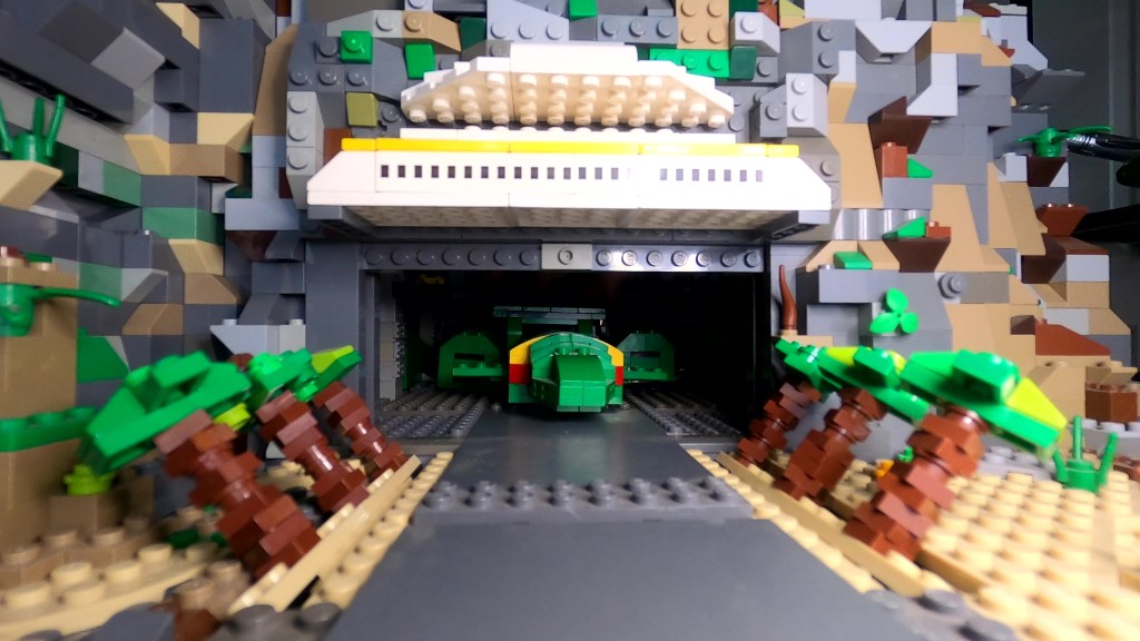 Thunderbird 2 rolls out of the hangar through the hidden cliff door and past the folding palm trees.